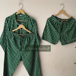 Può includere: Set pigiama a quadri verdi e bianchi, composto da camicia a maniche lunghe, pantaloni lunghi e pantaloncini. I pigiami sono appesi a grucce di legno. Rifiniture bianche.