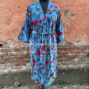 May include: A blue velvet robe with a floral and bird print. The robe has a tie belt and two pockets. "DHANLAXMI HANDICRAFTS" is printed on the robe.
