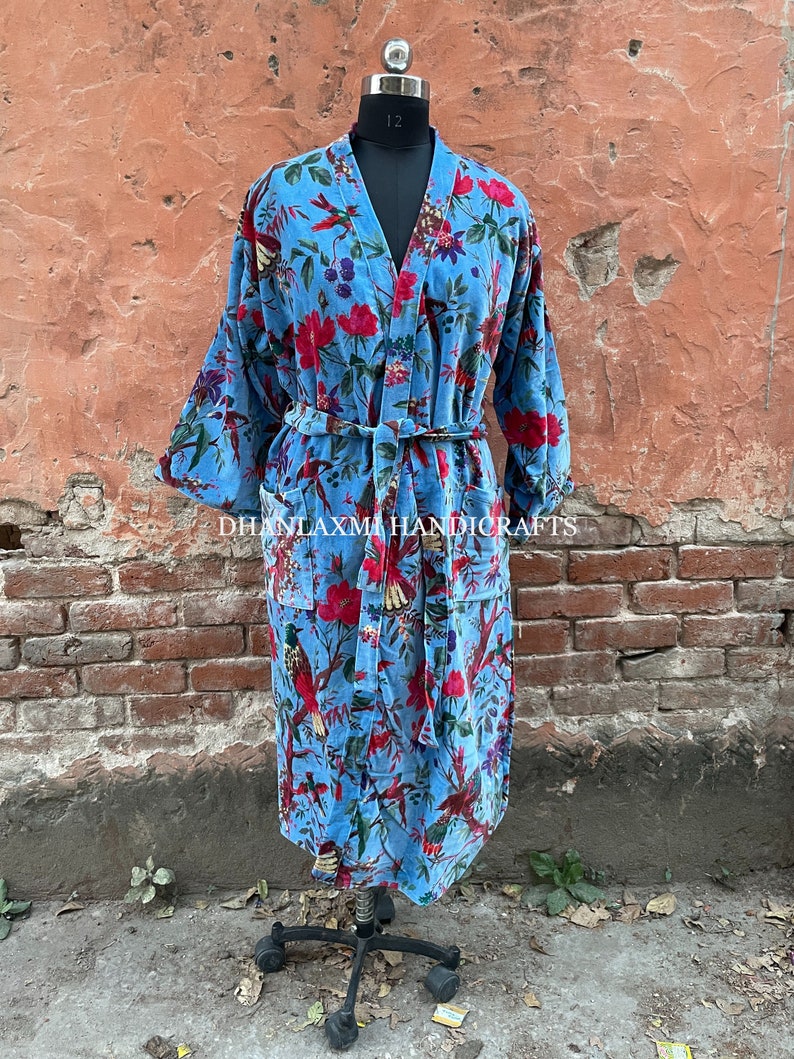 May include: A blue velvet robe with a floral and bird print. The robe has a tie belt and two pockets. "DHANLAXMI HANDICRAFTS" is printed on the robe.