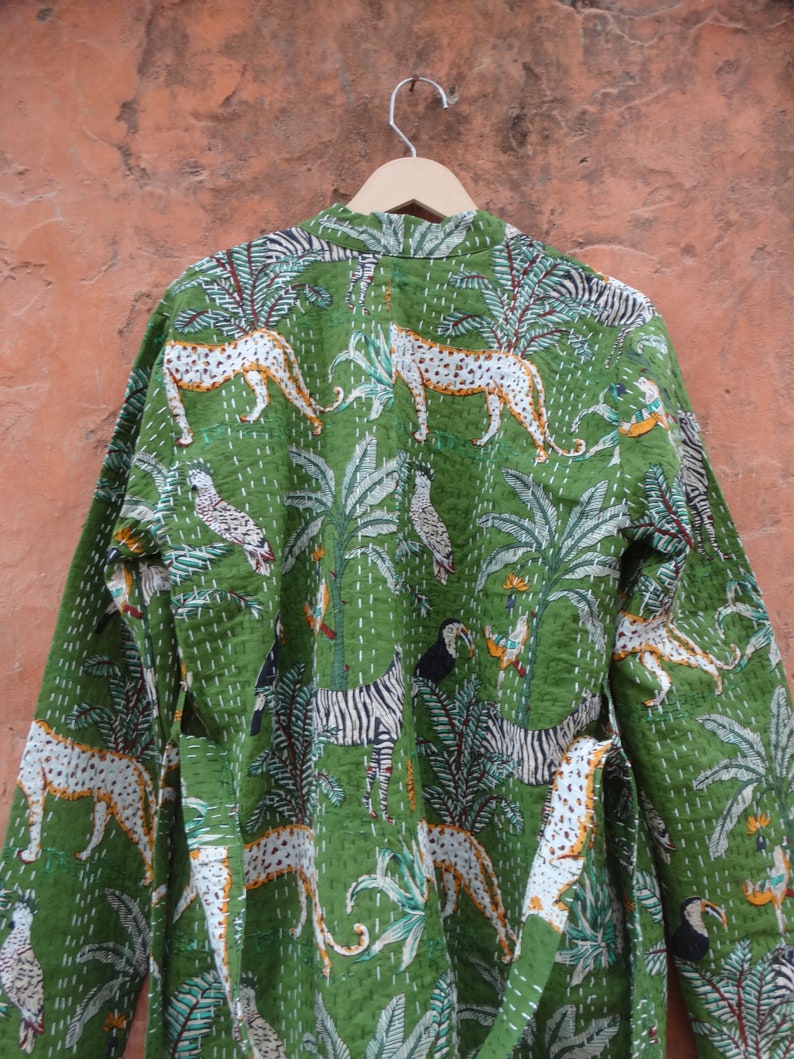 May include: A green cotton robe with a jungle print featuring zebras, leopards, toucans, and palm trees. The robe has a long sleeve and a tie belt.