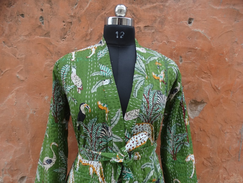 May include: A green cotton jacket with a floral and animal print. The jacket has a long sleeve and a tie belt. The print features toucans, zebras, and flamingos.