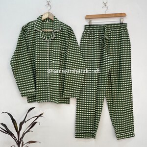 May include: Green and white checkered pajama set. The long-sleeved top has a button-down front and white trim. The matching pants have a drawstring waist. The set is hanging on a white wall. The text "@hanlaxmihandicraft" is visible.