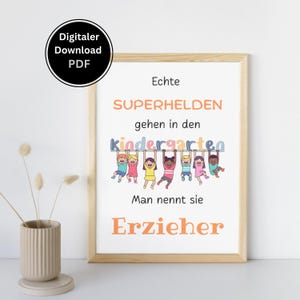 May include: A framed print with the text "Echte SUPERHELDEN gehen in den kindergarten Man nennt sie Erzieher." The print features a colorful illustration of children hanging from a banner. A digital download PDF is also available.