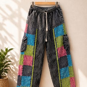 May include: Acid-wash black denim cargo pants featuring an elastic waistband with a white drawstring. The pants include side cargo pockets and colorful patchwork panels in shades of bright blue, lime green, and hot pink with a textured pattern.