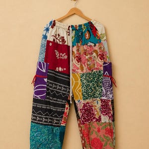 Peut inclure: Pantalon en patchwork composé de divers carrés de tissu colorés aux motifs floraux, géométriques et abstraits. Le pantalon présente une taille élastique avec un cordon de serrage blanc, des poches latérales avec des liens rouges et des chevilles resserrées.