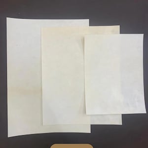 Może przedstawiać: Stos czterech prostokątnych arkuszy papieru w kolorze złamanej bieli, o różnych rozmiarach, ułożonych na ciemnobrązowej powierzchni. Słowo "Natural" jest wyświetlane na brązowej etykiecie na dole.
