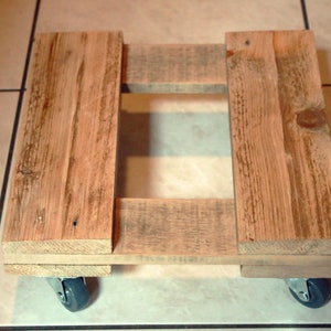 Może przedstawiać: Drewniana podstawa palety z czterema kołami, idealna do przemieszczania ciężkich przedmiotów w domu lub warsztacie.