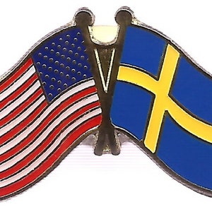 Puede incluir: Un pin con las banderas de Estados Unidos y Suecia. La bandera estadounidense tiene rayas rojas y blancas con un campo azul de estrellas blancas. La bandera sueca es azul con una cruz amarilla.