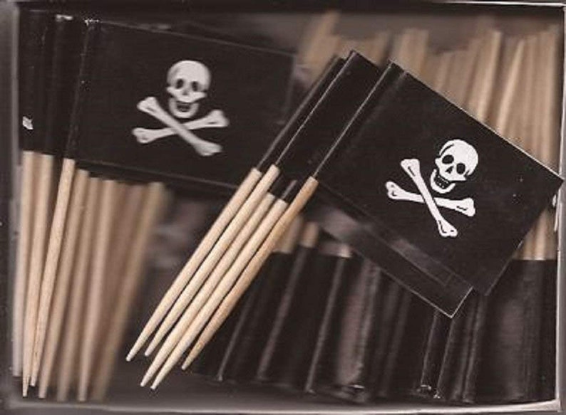 May include: A collection of pirate-themed toothpick flags. Each flag is black with a white skull and crossbones design. The flags are attached to wooden toothpicks, creating a fun and thematic party supply.