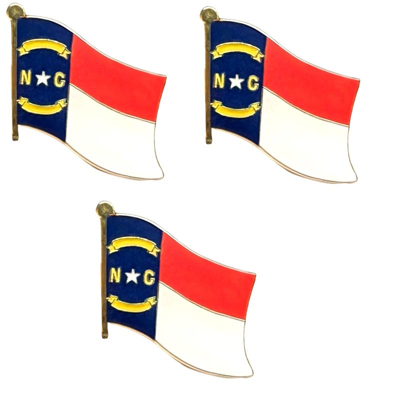 Puede incluir: Tres pines de solapa de metal con la forma de la bandera del estado de Carolina del Norte. Cada pin presenta una franja vertical azul con una estrella blanca entre las letras N y C, flanqueada por pergaminos amarillos y dos franjas horizontales en rojo y blanco.