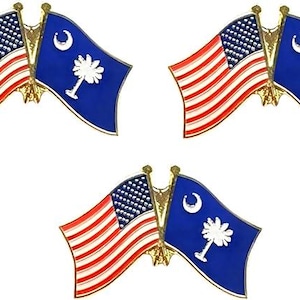 May include: Three gold-toned metal lapel pins, each featuring two crossed flags. One flag is the United States flag with red and white stripes and a blue canton with white stars. The other is the blue South Carolina state flag with a white crescent.