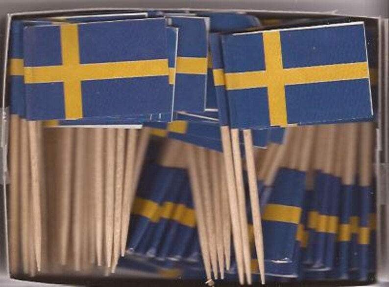 Puede incluir: Una caja llena de banderas suecas en palillos de dientes. Las banderas tienen un fondo azul con una cruz amarilla. Los palillos son de madera.