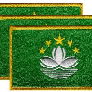 May include: Three embroidered patches featuring the flag of Macau. Each patch has a green background with a white lotus flower, five yellow stars, and a gold border. The patches are rectangular.