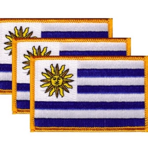 May include: Three embroidered patches featuring the flag of Uruguay. Each patch has a white background with blue stripes and a yellow sun emblem. The patches are rectangular with a gold border.