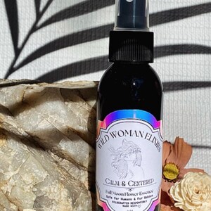 May include: A black glass bottle with a spray nozzle, labeled "WILD WOMAN ELIXIRS CALM & CENTERED Full Moon Flower Essence Safe for Humans & For Babies WILDCRAFTED RESPONSIBLY MADE WITH LOVE"