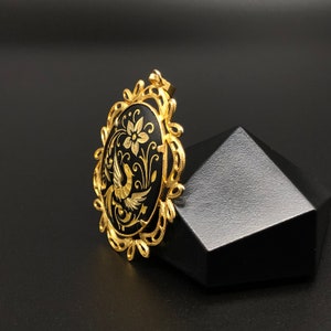 May include: A gold pendant with a black oval cameo featuring a stylized bird and floral design.
