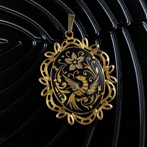 May include: A gold pendant with a black enamel oval featuring a gold bird and floral design.