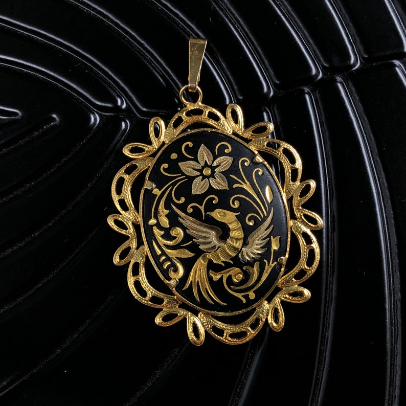 May include: A gold pendant with a black enamel oval featuring a gold bird and floral design.