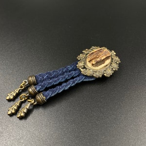 May include: A blue suede tassel pendant with a gold-toned metal frame and a brown antler accent. The pendant is attached to a blue suede cord.