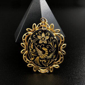 May include: Gold pendant with a black enamel oval featuring a detailed design of a bird with floral accents.