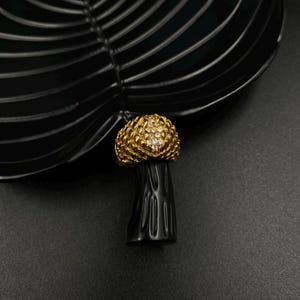 May include: A gold ring with a large, round, clear stone surrounded by smaller stones. The ring is on a black surface.