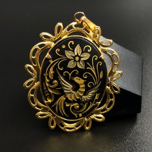 May include: A gold pendant with a black oval cameo featuring a gold bird and floral design.