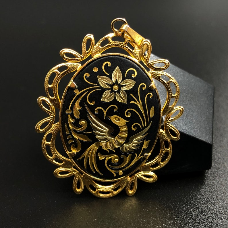May include: A gold pendant with a black oval cameo featuring a gold bird and floral design.