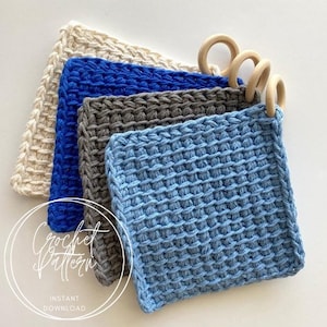 May include: Four crocheted dishcloths in different colors: beige, blue, gray, and light blue. The dishcloths are stacked on top of each other and have wooden rings attached to the top.