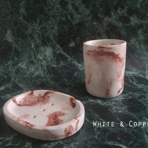 May include: White and copper bathroom set with a soap dish and a tumbler. Both pieces have a marbled design with white and copper accents.