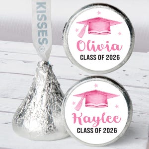 May include: A wrapped Hershey's Kiss with a white ribbon and two graduation-themed stickers. The stickers feature a pink graduation cap, the name "Olivia" and "Kaylee", and the text "CLASS OF 2026" in pink.