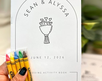 May include: A white wedding activity book with black text reading Sean & Alyssa, June 12, 2026, and Wedding Activity Book, featuring a line drawing of a heart bouquet inside an arch. A small clear plastic bag contains five yellow crayons.