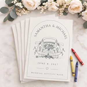 May include: A stack of white wedding activity books featuring a black line drawing of a car with a Just Married sign, ribbons, and cans. The text reads Samantha & Michael, June 4, 2027, and Wedding Activity Book. Three crayons in red, yellow, and blue lie nearby.