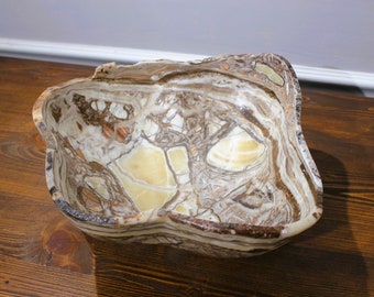 May include: A large, irregularly shaped bowl carved from brown and white onyx. The bowl has a natural, organic shape and a smooth, polished finish.