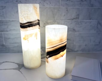 May include: Two white onyx lamps with black and brown stripes. The lamps are on a white countertop.