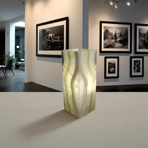 Puede incluir: Una l&aacute;mpara rectangular iluminada hecha de piedra transl&uacute;cida y en capas. La l&aacute;mpara tiene una combinaci&oacute;n de colores verde claro y blanco con un patr&oacute;n natural y org&aacute;nico. La l&aacute;mpara est&aacute; sobre una superficie blanca, proyectando una sombra.