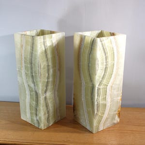 Puede incluir: Dos jarrones rectangulares de &oacute;nix verde claro con una parte superior hexagonal. Los jarrones tienen un patr&oacute;n natural y en capas de verde y blanco, y se exhiben sobre una superficie de madera.