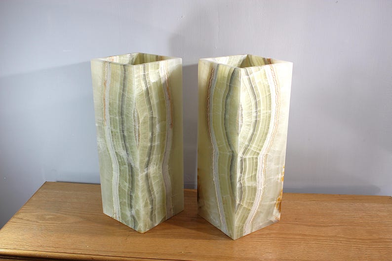 Puede incluir: Dos jarrones rectangulares de &oacute;nix verde claro con una parte superior hexagonal. Los jarrones tienen un patr&oacute;n natural y en capas de verde y blanco, y se exhiben sobre una superficie de madera.