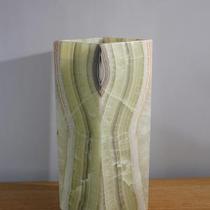 Puede incluir: Un jarr&oacute;n alto y rectangular de &oacute;nix verde con un patr&oacute;n &uacute;nico en capas. El jarr&oacute;n tiene una parte superior e inferior cuadradas, y la piedra natural muestra tonos de verde, blanco y marr&oacute;n. El jarr&oacute;n mide unos 30 cm de alto.