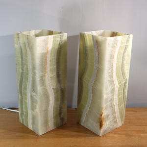 Puede incluir: Dos l&aacute;mparas rectangulares de &oacute;nix en tonos verde claro y crema. Las l&aacute;mparas tienen un aspecto veteado y marmolado con finas vetas marrones y anaranjadas. Se colocan sobre una superficie de madera.