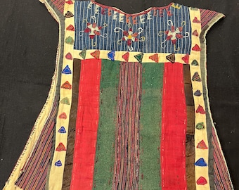 May include: A colorful, handmade tunic with a patchwork design. The top features a blue striped yoke with embroidered floral patterns. The body of the tunic is composed of vertical stripes in red, green, and brown. The edges are trimmed with patterned fabric.