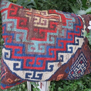 May include: A decorative pillow with a geometric pattern in shades of red, blue, brown, and white. The pattern is a repeating design of squares and triangles.