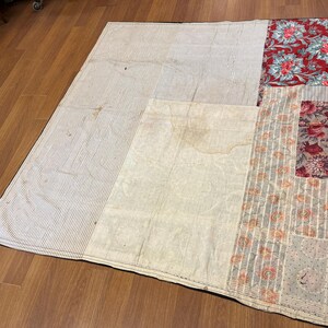 May include: A patchwork quilt with various fabric patterns. The quilt features sections of white and gray striped fabric, floral prints in red and pink, and a cream-colored central panel. The quilt is laid out on a wooden floor.