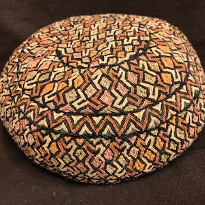 May include: A round, black, brown, and pink patterned hat with a geometric design.