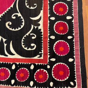 May include: A close-up of a textile with a vibrant design. The piece features a black, white, and red color scheme. The design includes floral and geometric patterns, with a black border and a red and pink background.