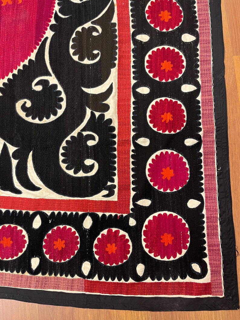 May include: A close-up of a textile with a vibrant design. The piece features a black, white, and red color scheme. The design includes floral and geometric patterns, with a black border and a red and pink background.