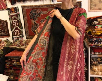 May include: A long, open-front coat featuring a deep red exterior with white embroidered geometric and floral patterns. The interior lining displays a contrasting multi-colored paisley print in shades of red, blue, and cream. The garment has short sleeves.