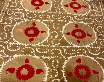 May include: A large textile wall hanging or coverlet featuring a repeating pattern of six prominent circular medallions in vibrant red against a tan background. The design includes intricate white swirling floral motifs and paisley shapes.