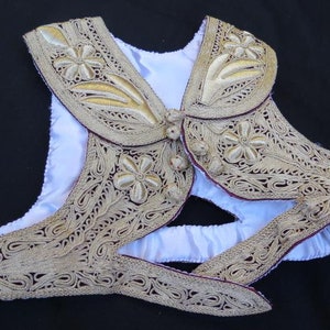 May include: A white vest with a gold and burgundy embroidered collar and trim. The embroidery features floral and leaf designs.