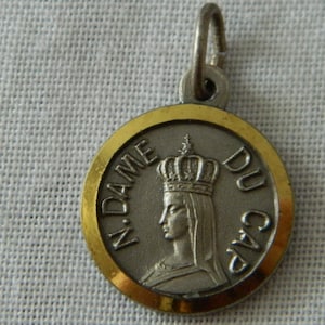 May include: A silver and gold religious medal with a depiction of a crowned woman and the text "N. DAME DU GAP".