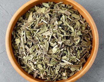 May include: A round wooden bowl filled with a mixture of dried green herbs and thin, light-colored stalks. The contents consist of various small, fragmented botanical pieces in shades of olive, sage, and pale yellow, creating a textured blend.